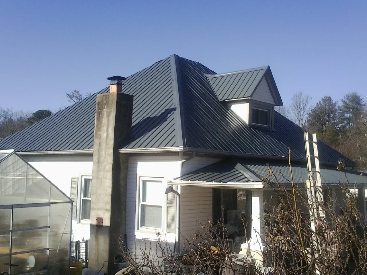 Dark blue standing seam metal roof on a white farmhouse with dormer — Slate & Tile Roof Repair by Roofing Brothers in Lawrence