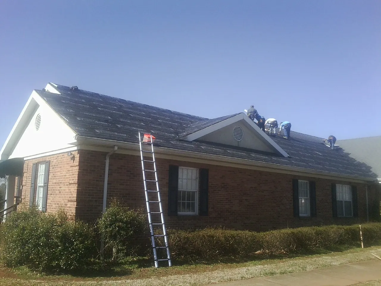 Crew tearing shingles off a brick ranch roof with a ladder set — Metal Roof Repair work by our crew in Lawrence