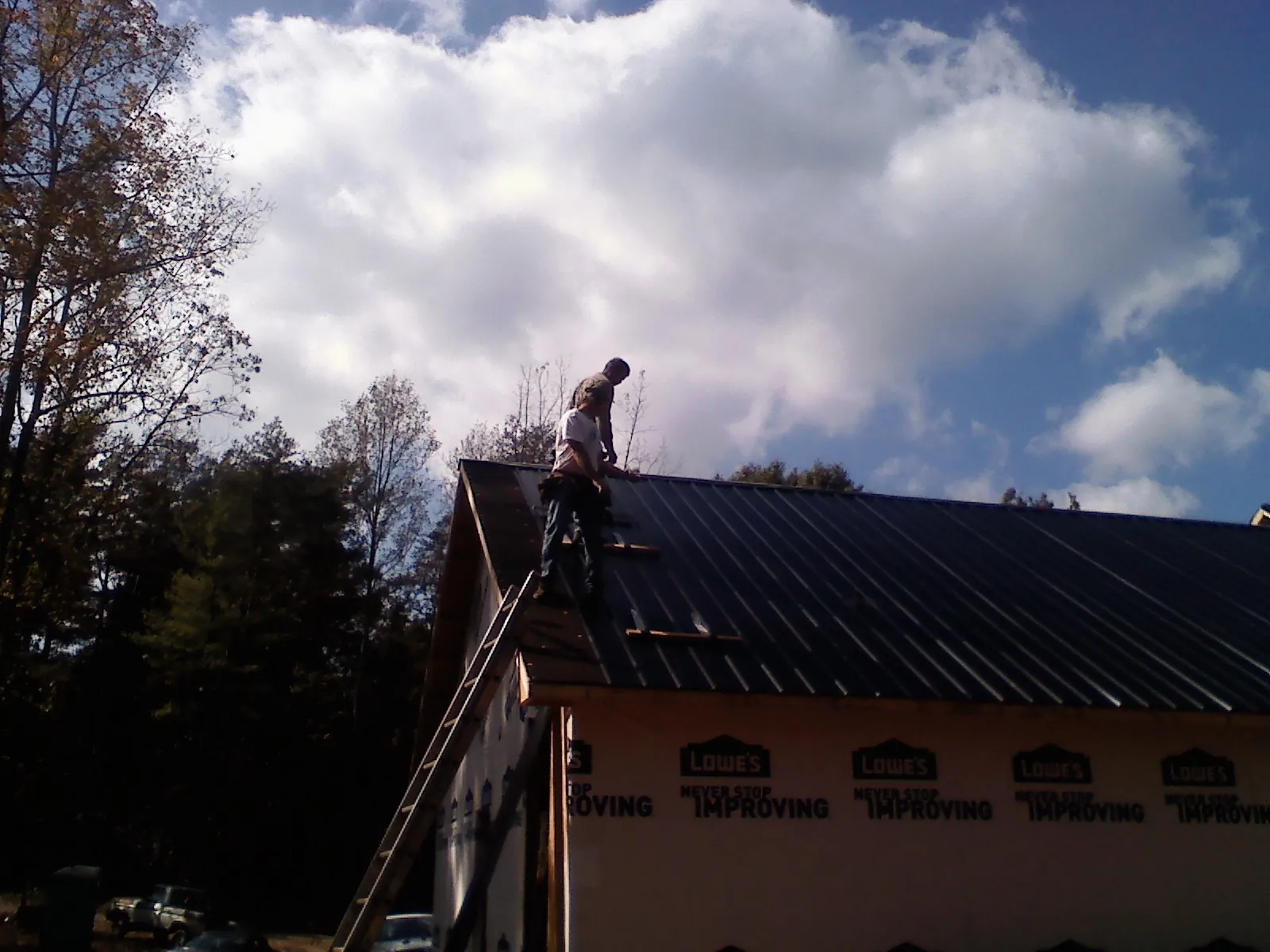 Roofer fastening dark metal panels high against a cloudy sky, from a Roof Inspection job in Lawrence